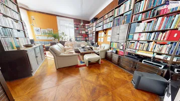 Geräumiges Wohnzimmer mit umfangreichen Bücherregalen, Parkettboden und gemütlicher Sitzecke.