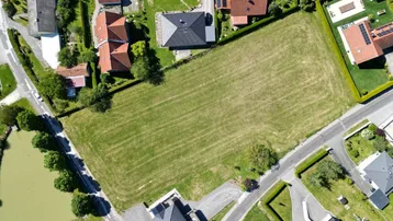 Luftaufnahme eines großen, grünen Grundstücks in ländlicher Umgebung, umgeben von Wohnhäusern und einem Teich.