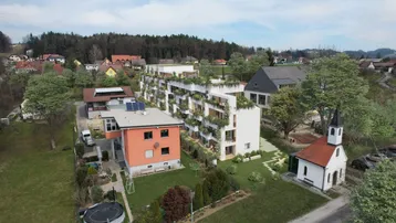 Luftaufnahme eines modernen Wohnkomplexes mit begrünten Fassaden und Balkonen in ländlicher Umgebung.