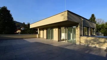 Große, geflieste Dachterrasse mit Blick auf die Umgebung und das moderne Gebäude unter blauem Himmel.