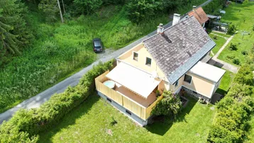Vogelperspektive des Hauses mit ausgefahrener Markise über einem Balkon und umgebendem Garten.