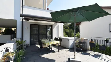 Geräumige Sonnenterrasse mit Esstisch, Sonnenschirm und Blick ins Grüne, ideal für entspannte Stunden im Freien.