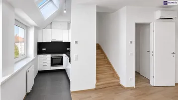 Heller offener Wohnbereich mit integrierter Küche, Holztreppe und Dachfenstern für viel Tageslicht.