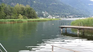 Malerischer Blick auf den See mit bewaldeten Bergen im Hintergrund und einem kleinen Steg.