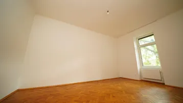 Helles Zimmer mit Fischgrätparkettboden und einem Fenster mit Blick ins Grüne, ideal als Schlafzimmer.
