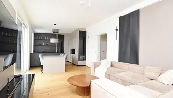 Offener Wohn-Essbereich mit moderner Küche, hellem Holzboden und beigem Sofa.