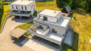 Luftaufnahme von modernen Gebäuden mit Flachdächern und Terrassen, eingebettet in grüne Landschaft.