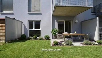Außenbereich mit Rasenfläche, möblierter Terrasse und Balkon am modernen Gebäude.