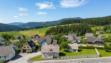 Malerische Luftaufnahme eines Dorfes in ländlicher Umgebung mit grünen Hügeln und Wäldern.