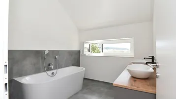 Modernes Badezimmer mit freistehender Badewanne, Einzelwaschbecken und Fenster mit Blick ins Grüne.