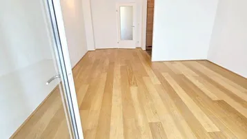 Heller, leerer Raum mit neuem Holzparkettboden und Zugang zu einem weiteren Zimmer.