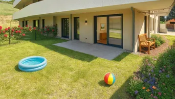 Gepflegter Gartenbereich mit Rasenfläche, kleiner Terrasse und Zugang zum Gebäude.