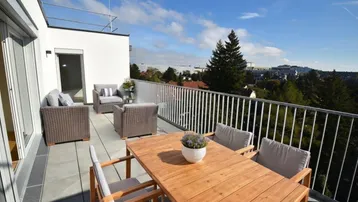 Geräumige Dachterrasse mit Holztisch, bequemen Loungemöbeln und weitem Blick ins Grüne unter blauem Himmel.
