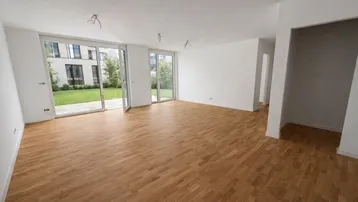 Helles Wohnzimmer mit Parkettboden und großen Glastüren, die zum Garten führen.