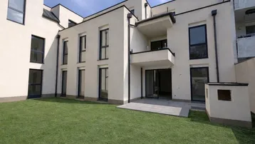 Modernes Mehrfamilienhaus mit gepflegtem Rasen und einer Terrasse im Erdgeschoss.