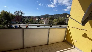 Sonniger Balkon mit Fliesenboden und weitem Blick über die grüne Landschaft.