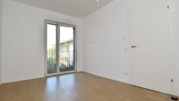 Leerer Raum mit hellem Holzboden und Zugang zu einem französischen Balkon.