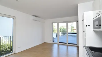 Helles Zimmer mit Holzboden, integrierter Küchenzeile und Zugang zu einer Terrasse.