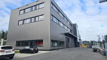 Modernes Geschäftsgebäude mit dunkler Fassade und großen Fenstern unter bewölktem Himmel.