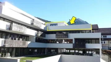 Modernes Apartmentgebäude mit Balkonen und Bergblick, die oberste Etage ist hervorgehoben.