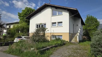 Freistehendes Einfamilienhaus mit heller Fassade, Satteldach und einem Vorgartenbereich.