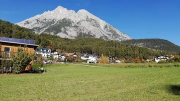 Grüne Wiese mit Blick auf majestätische Berge und umliegende Häuser unter blauem Himmel.