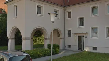 Mehrfamilienhaus mit heller Fassade, roten Ziegeldächern und einem Bogenzugang im Vordergrund.