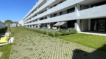 Moderne Wohnanlage mit Balkonen und begrünten Terrassen im Erdgeschoss, umgeben von Rasenflächen.