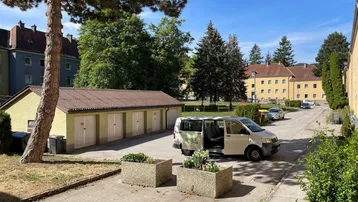Außenansicht einer Wohnanlage mit Garagenreihe, Parkplätzen und viel Grün unter blauem Himmel.