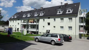 Mehrfamilienhaus mit hellgrüner Fassade, Balkonen und Parkplätzen im Freien.