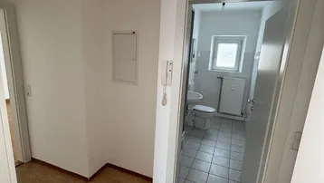 Flur mit Linoleumboden und Blick in ein gefliestes Badezimmer mit Fenster.