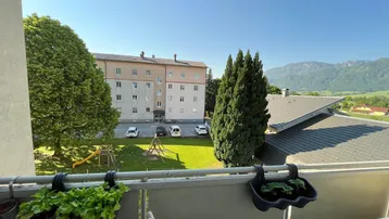 Blick vom Balkon auf den Innenhof mit Spielplatz und die umliegende Berglandschaft.