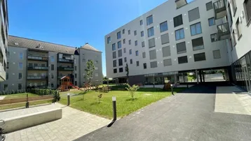 Moderne Wohngebäude mit gepflegtem Innenhof, Rasenflächen und Kinderspielplatz unter blauem Himmel.