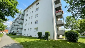 Mehrfamilienhaus mit weißer Fassade, Balkonen und gepflegter Grünanlage im Freien.