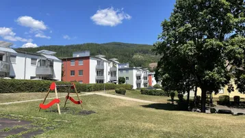 Gemeinschaftlicher Gartenbereich mit Spielplatz und Bäumen, umgeben von Wohngebäuden.