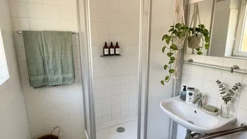 Helles Badezimmer mit Duschkabine, Waschbecken und weißen Fliesenboden.