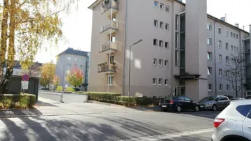 Mehrfamilienhaus mit moderner Fassade, Balkonen und Parkplätzen im Freien.