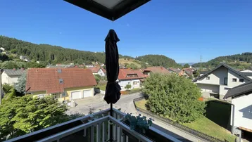 Sonnenverwöhnter Balkon mit Blick auf die umliegende Wohnsiedlung und bewaldete Hügel.