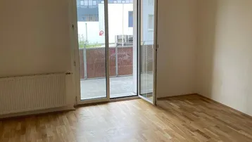 Helles Zimmer mit Parkettboden und Zugang zu einem Balkon, ideal für Wohn- oder Schlafbereich.