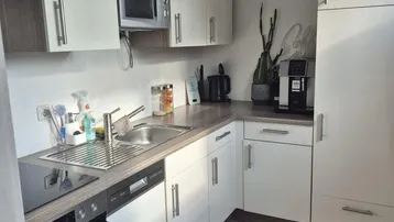 Moderne Küche mit weißen Schränken, integrierten Geräten und Spülbecken in gepflegtem Zustand.