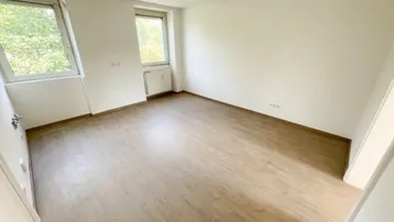 Helles Zimmer mit Laminatboden und zwei Fenstern, das viel Tageslicht hereinlässt.