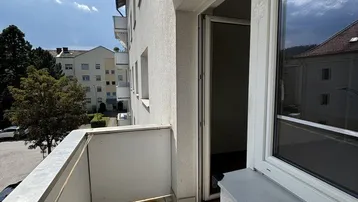 Heller Balkon mit Fliesenboden und Blick auf die umliegenden Gebäude und Bäume.