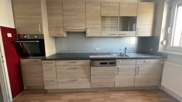 Moderne Einbauküche mit hellen Holzfronten, schwarzer Arbeitsplatte und integrierten Geräten.