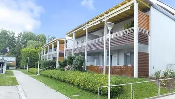 Mehrfamilienhaus mit mehreren Balkonen und gepflegter Grünanlage unter blauem Himmel.