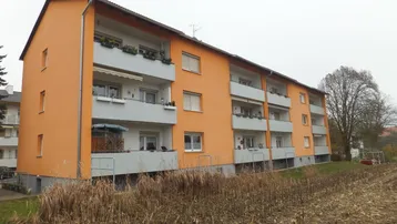 Orangefarbenes Mehrfamilienhaus mit Balkonen und Blick auf ein Feld.