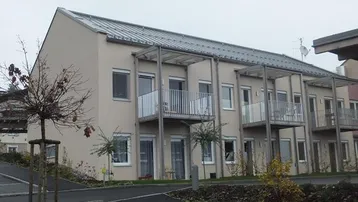 Modernes Mehrfamilienhaus mit heller Fassade und mehreren Balkonen, umgeben von Grünflächen.