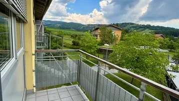 Geräumiger Balkon mit Fliesenboden und Metallgeländer, bietet einen weiten Blick ins Grüne.