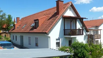 Gepflegtes Einfamilienhaus mit rotem Ziegeldach, weißer Fassade und kleinem Balkon.