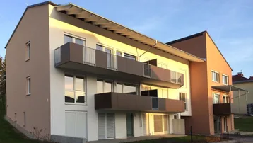 Modernes Mehrfamilienhaus mit mehreren Balkonen, großen Fenstern und einer Kombination aus hellen und erdigen Fassadenfarben.