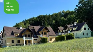 Reihenhäuser in ländlicher Umgebung mit grüner Hügellandschaft und Wald im Hintergrund.